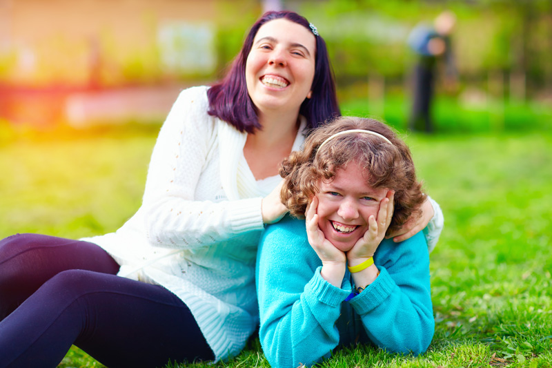 Two friends smiling while laying in grass.