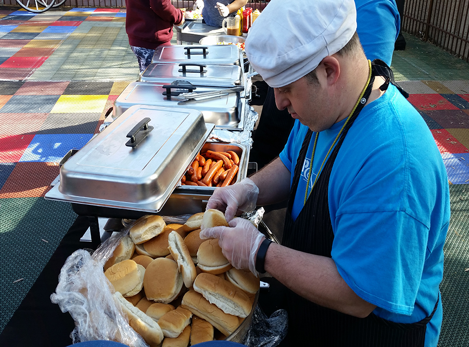 A man preparing hotdog and hamburger buns at an outdoor picnic.